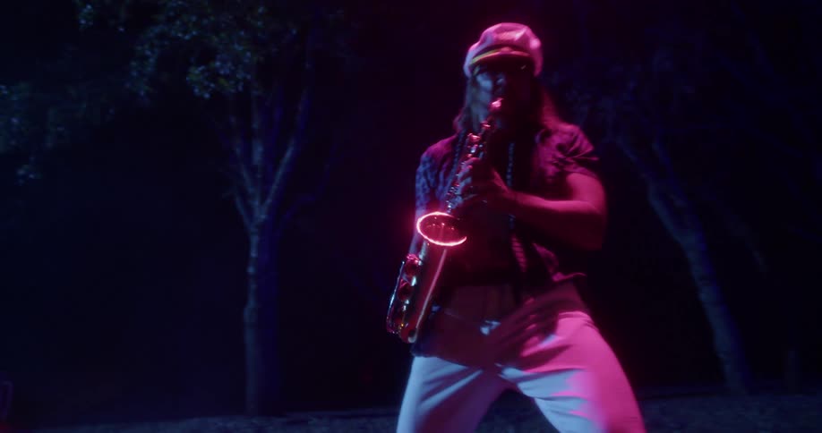 A man bends forward and backward as he plays the saxophone outside at night