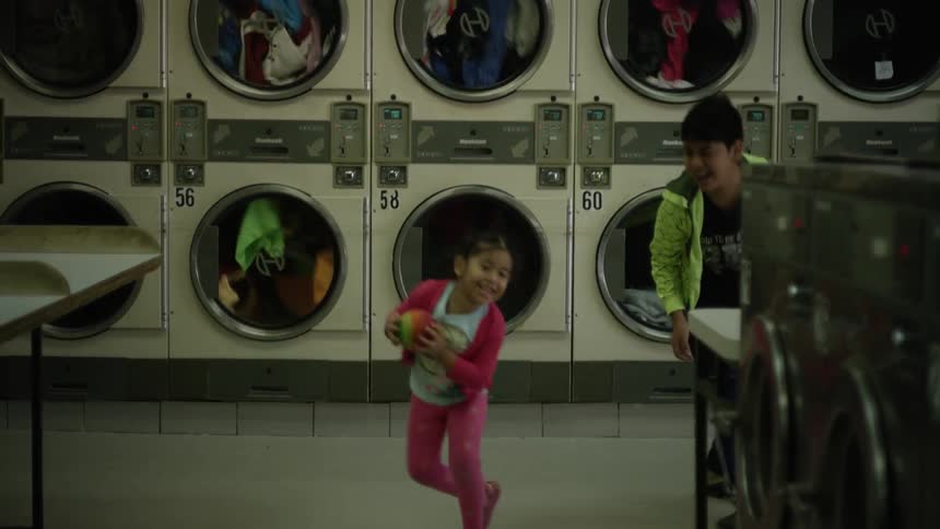 Two children play in front of a stack of dryers at a laundromat