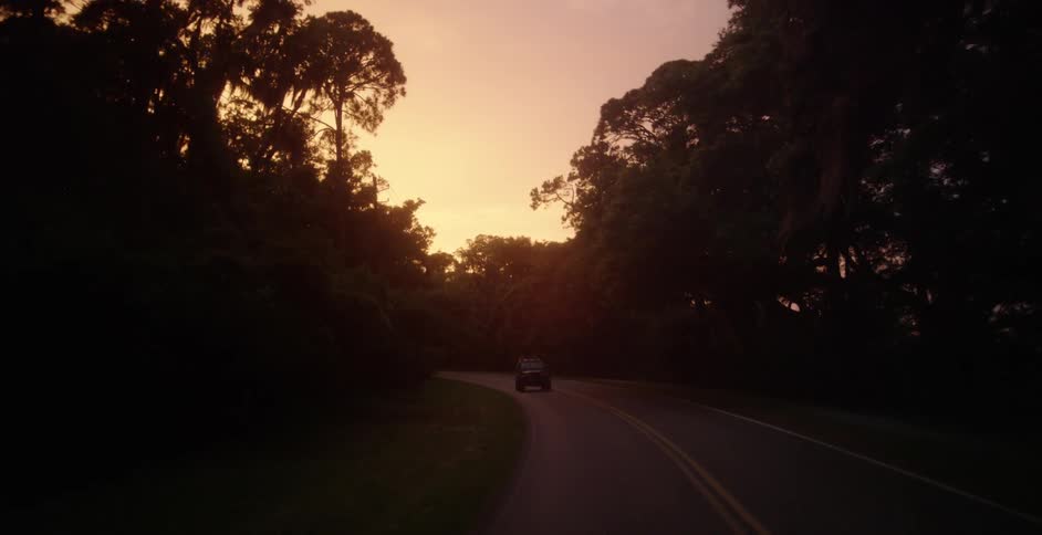 An suv drives down a country road at dusk
