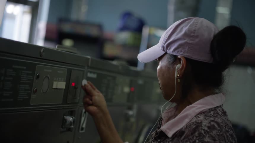 A woman in a pink hat puts quarters into a washing machine