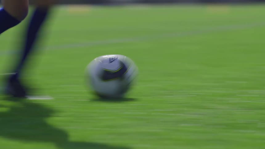 An athlete kicks a soccer ball across a soccer field