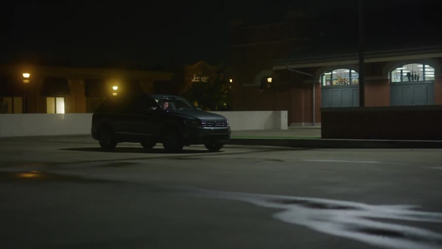 Man sitting inside a car parked in a parking lot at night