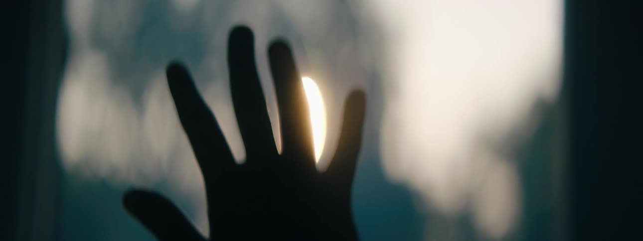 A person holds their hand up in front of the sun which creates a silhouette
