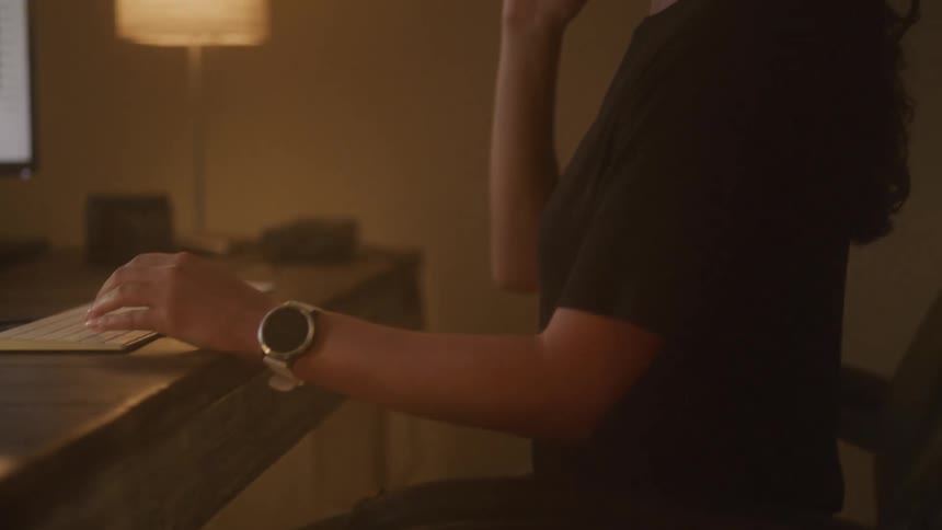 Woman sitting at desk consults computer screen while talking on mobile phone