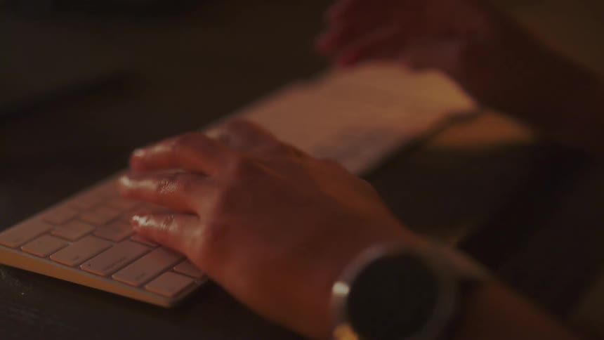 Woman wearing large wristwatch types on white computer keyboard