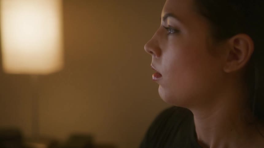 A dark haired woman talking on a cell phone indoors near a glowing lamp