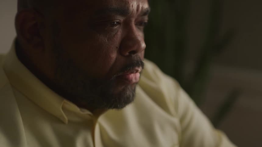 Man on a dimly lit room sits looking thoughtfully at something