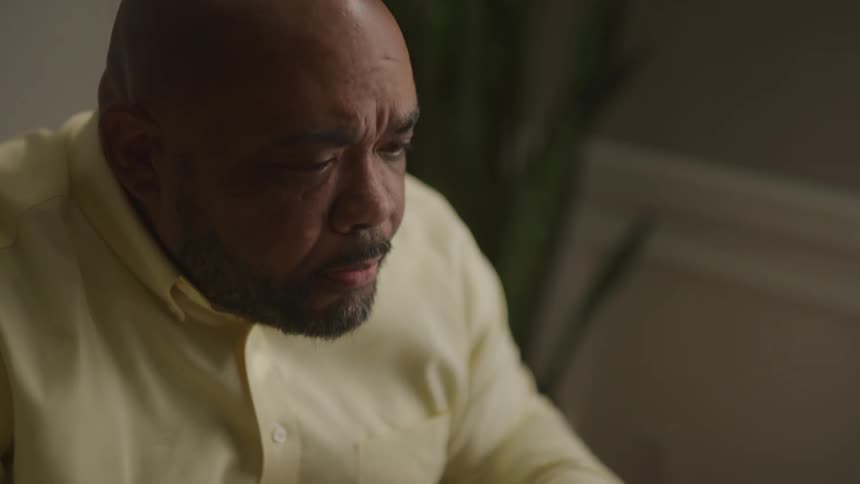 A man moves his head to read something out of frame while sitting indoors