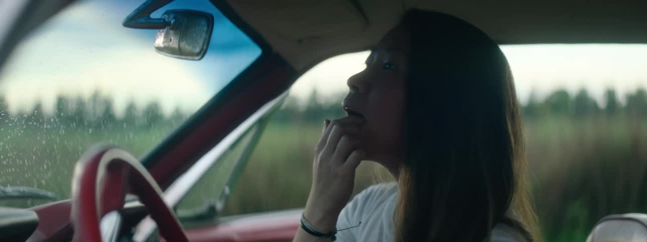 A woman is putting on lip gloss in the rearview mirror