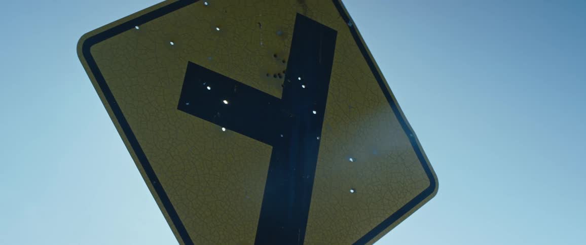 A traffic sign with bullet holes with sunlight shining through