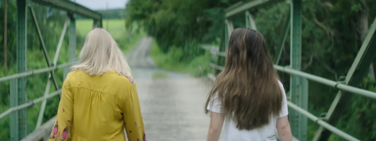 Two women walk briskly together across a small single lane bridge