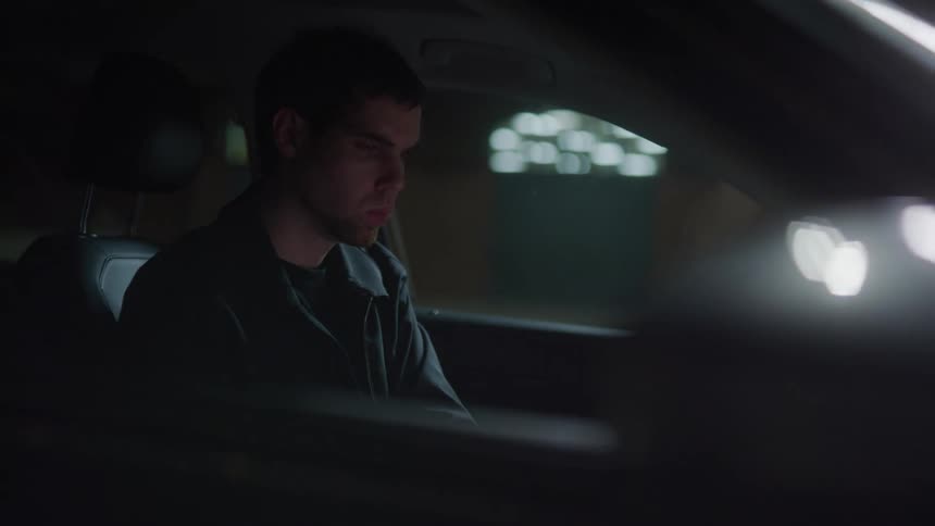 A man sits inside his vehicle in a parking lot at night