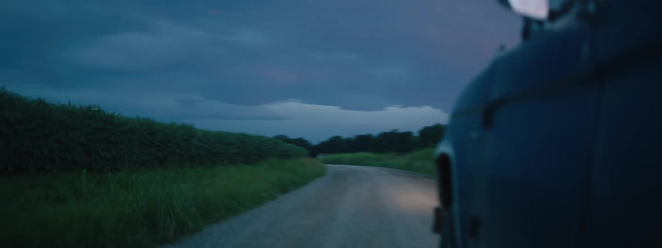 A vehicle driving on a dirt road with trees the sky and clouds in the background