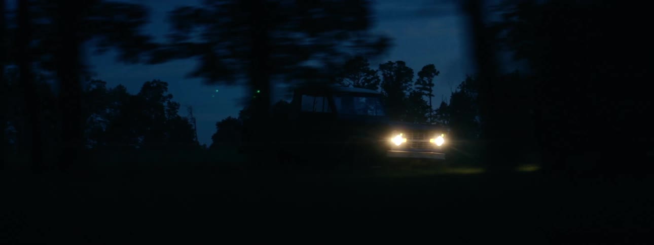 Pickup truck with headlights on driving through the trees in the countryside at night