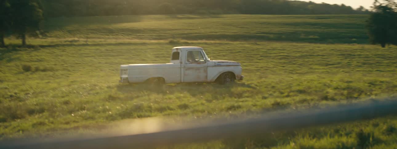 A truck driving and spinning out on a field with trees the sky and clouds in the background