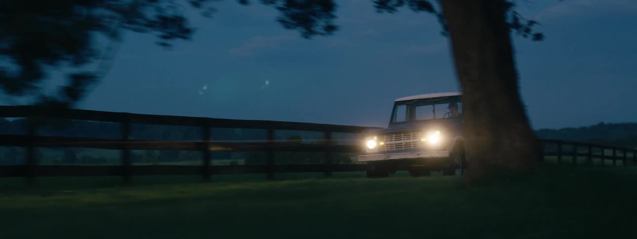 An old pickup truck drives along a bumpy dirt road in a rural setting