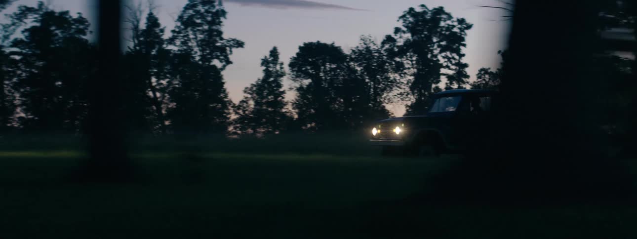 A pickup truck drives on the dirt road past the forest