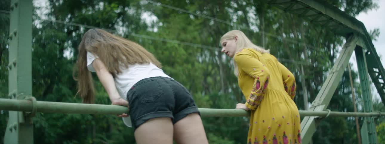 Two women lean on the railing of a bridge and look over it