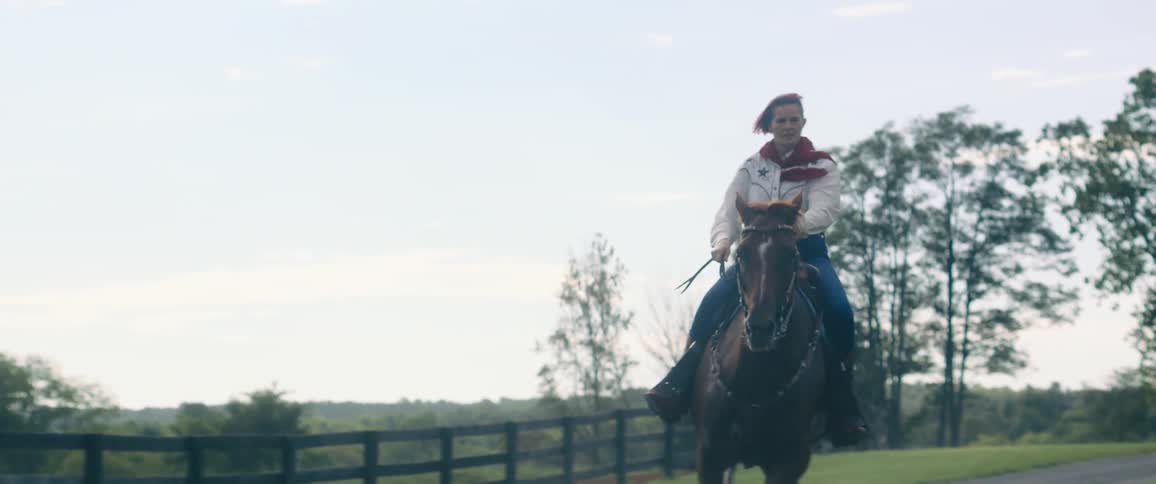 A woman rides a galloping horse on a path near grass and trees