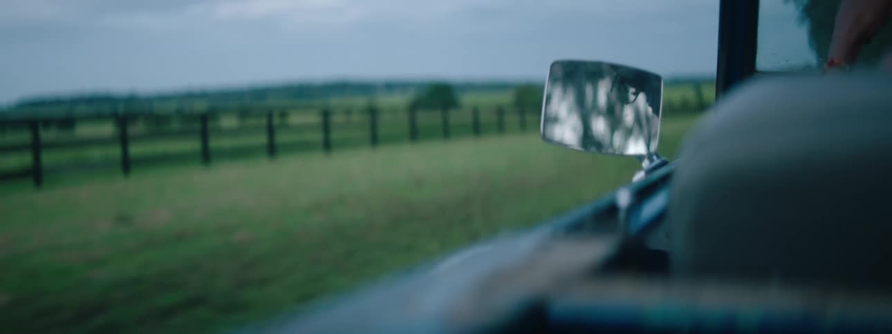 A vehicle is driving past the long green pasture