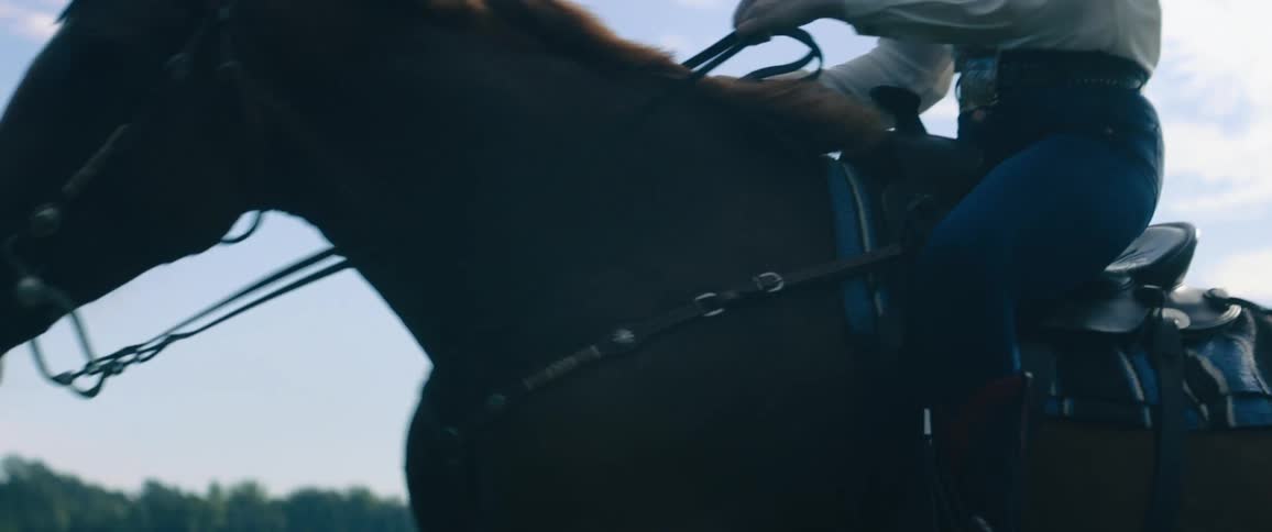 A person riding a horse on a track with trees the sky and clouds in the background