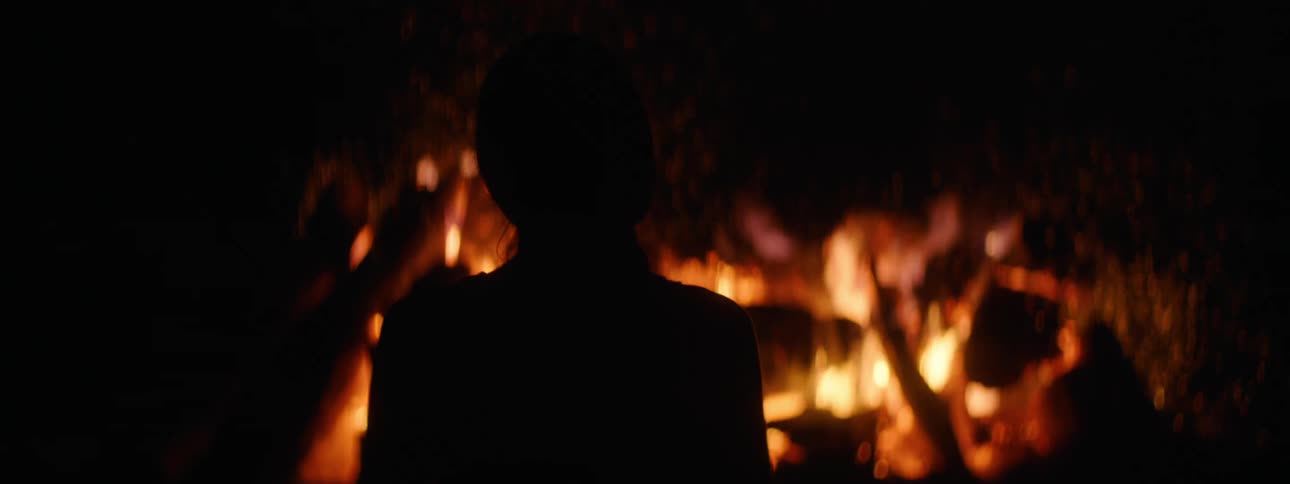 Silhouette of a short haired woman standing in front of a great bonfire at night