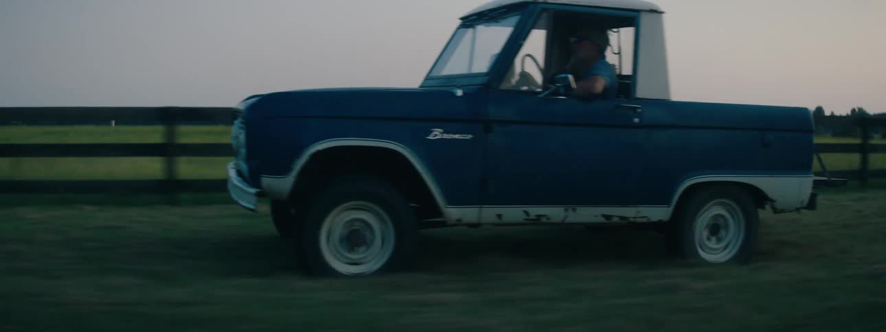 Father drives truck with short bed along grass covered path paralleling fence enclosing pasture