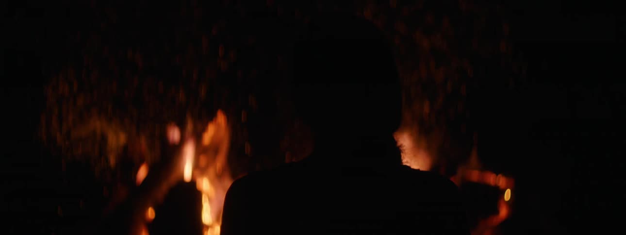 A silhouette of a person with a bonfire with smoke and embers in the background