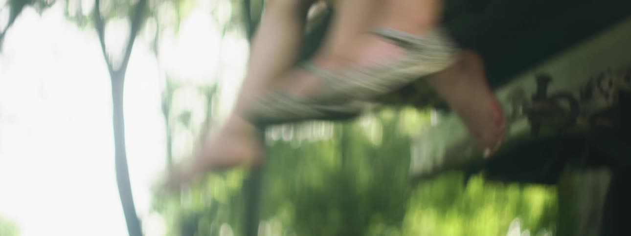 Two children sit and swing their legs over the side of a platform outdoors
