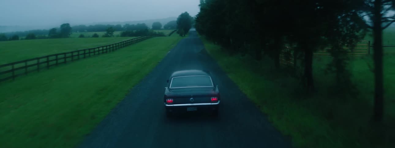 A car is driving down a road in a rural area