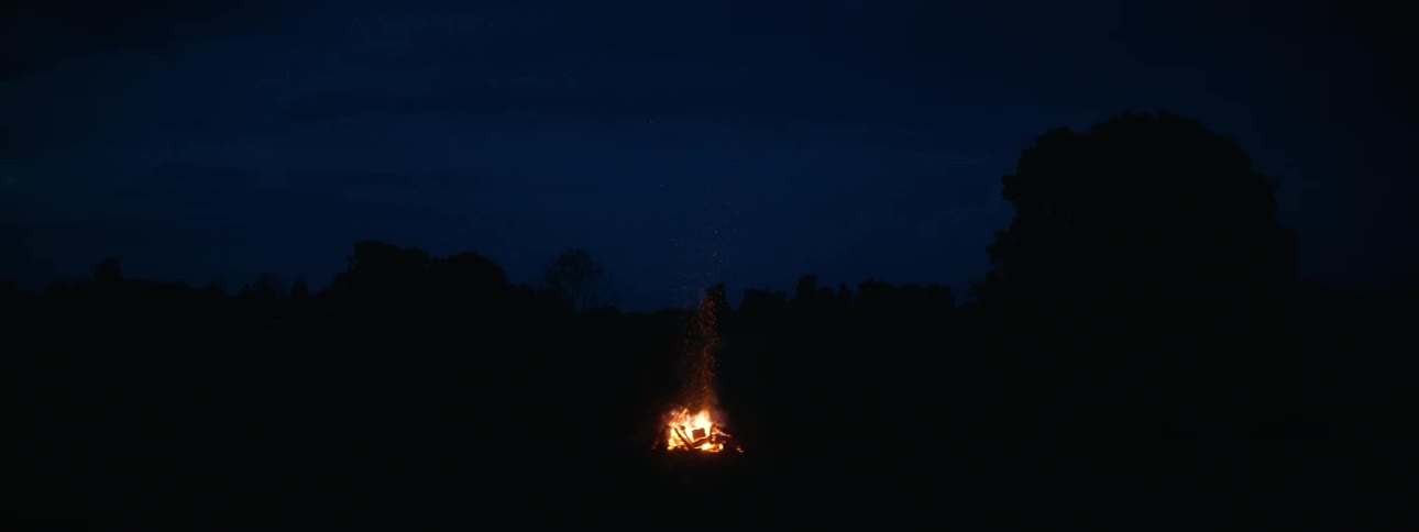 Far in the distance a fire is burning in a field at nighttime