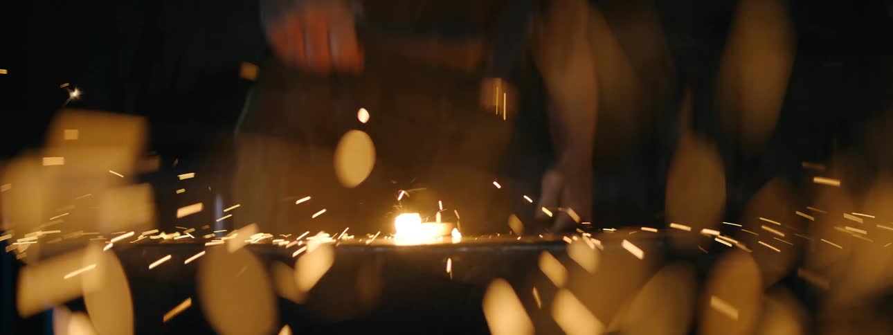 Female smith wearing leather apron hammers hot glowing metal on anvil
