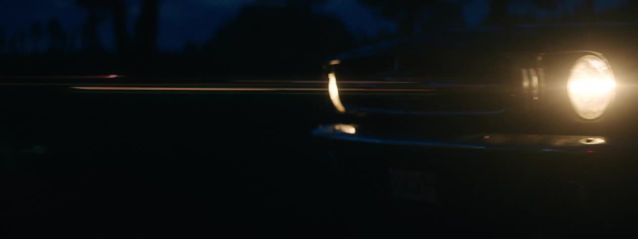 The bright headlights of a car as it travels through country road at night