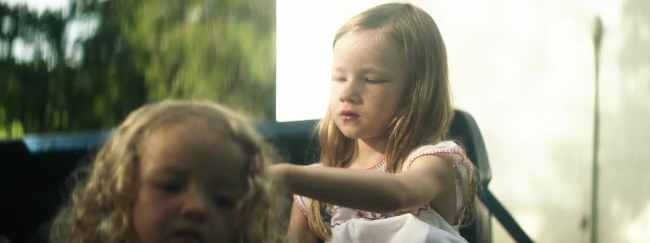 A girl brushes the hair of a younger girl while sitting in the bed of an old truck