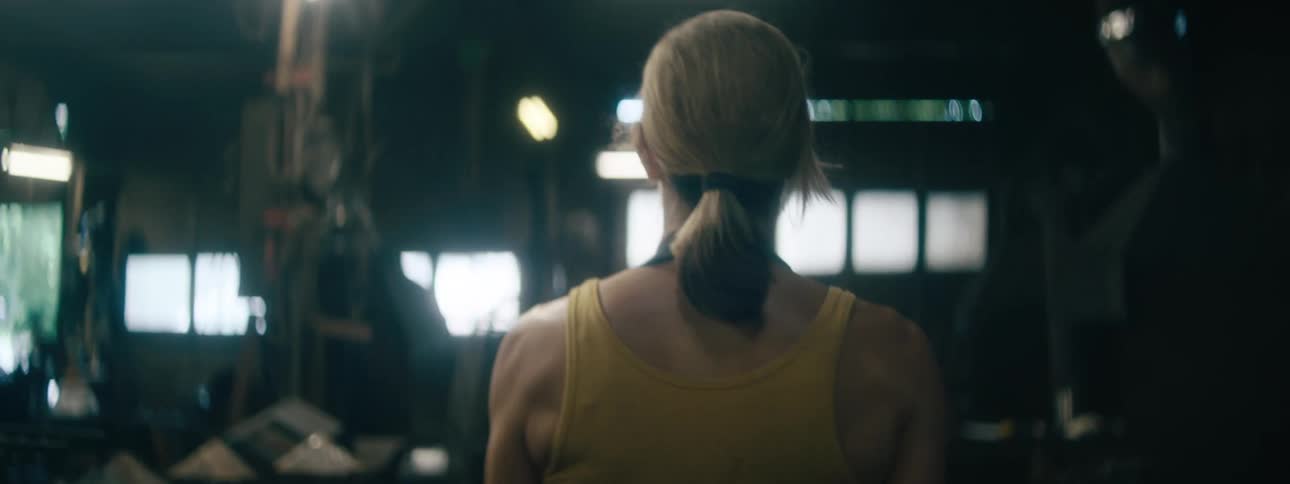 Muscles in a womans back and shoulders ripple as she walks through a garage