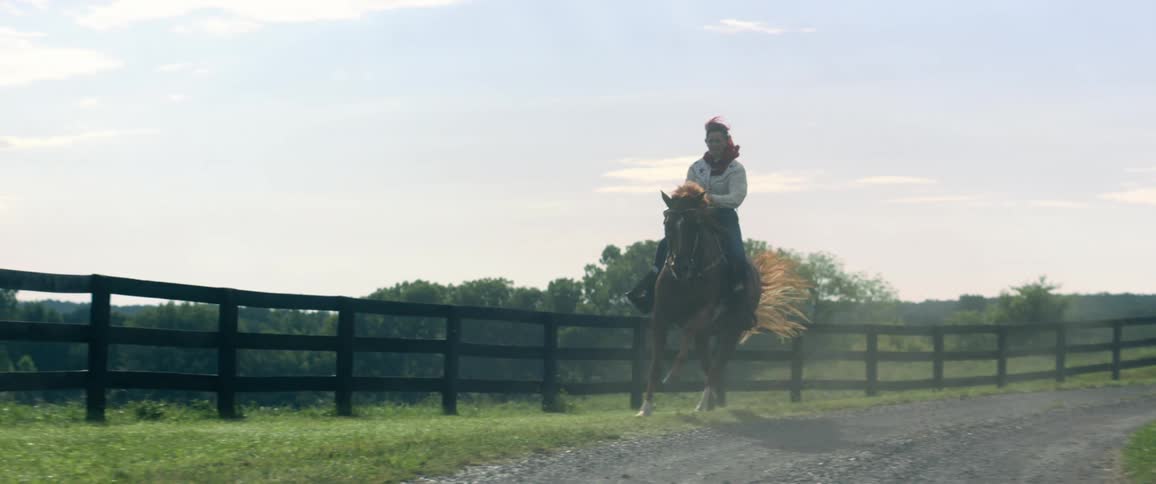 A woman riding a horse on a track with trees the sky and clouds in the background