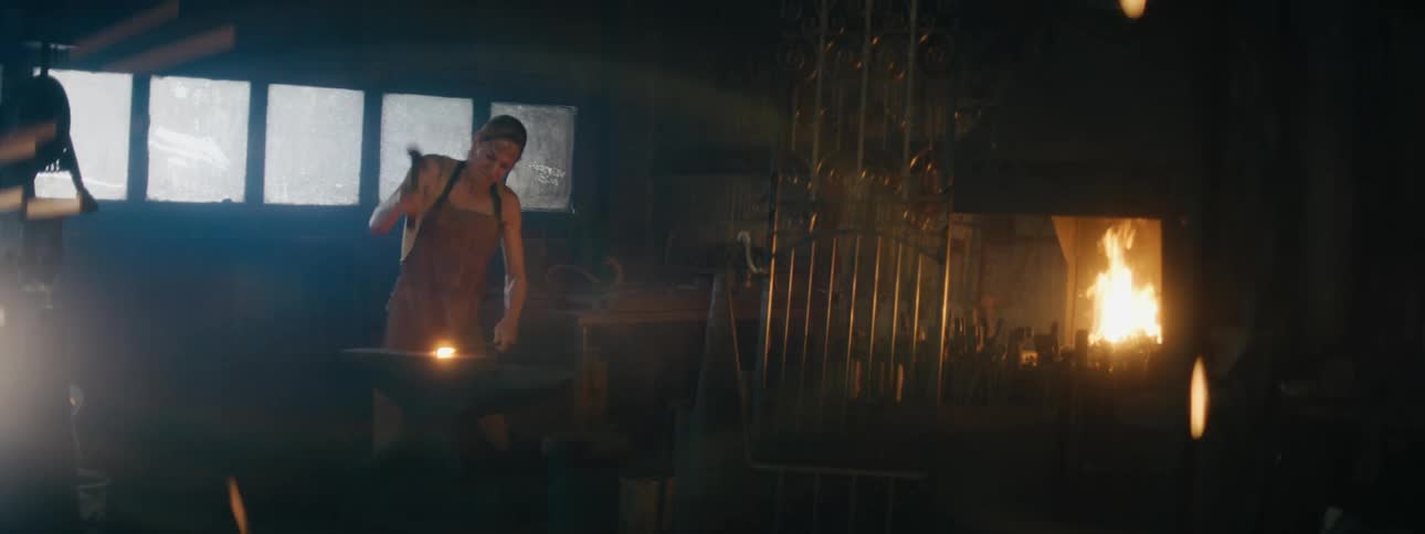 A woman blacksmith working on a something at an anvil