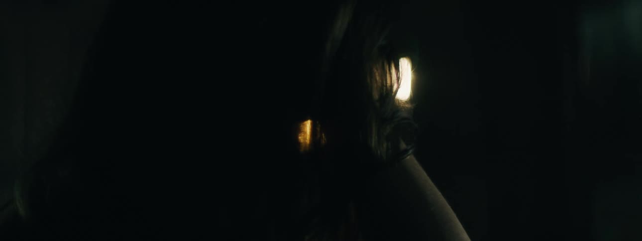 A woman in a dark room is looking through a hole with a shining bright light