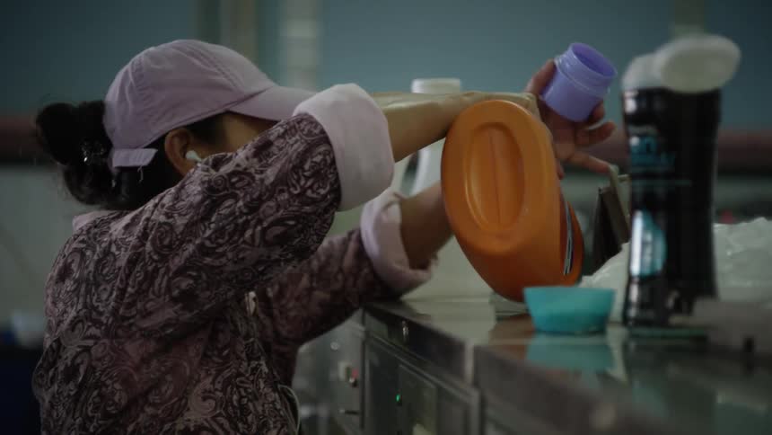 A woman pours orange soap into a washing machine