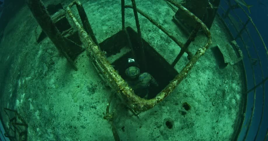 A scuba diver is exploring a sunken cylinder underwater