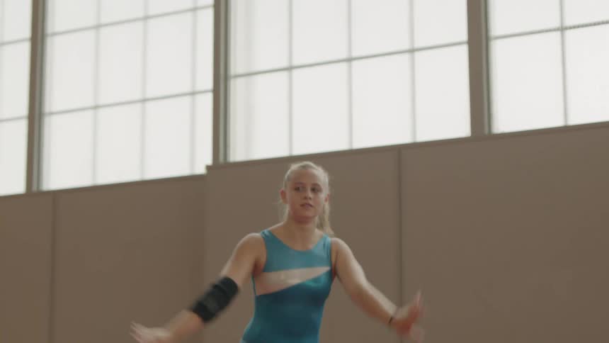 A young woman does a flip and lands her stand in a gymnasium