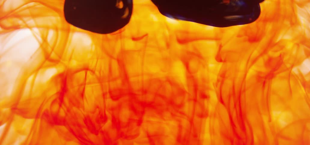 Dark red liquid slowly falls into an orange smoky looking background