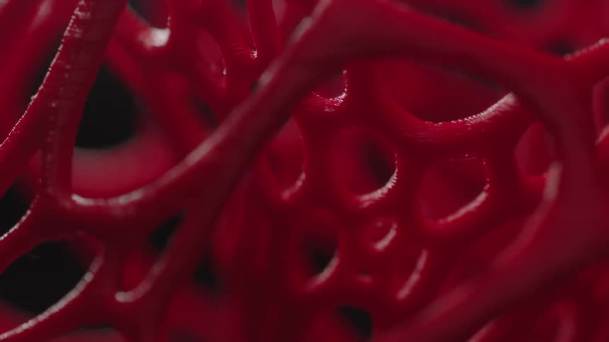 A lattice of smooth red fibers has light shined upon it in a darkened area