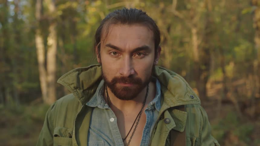Man wearing green jacket looks up and stands staring in woods