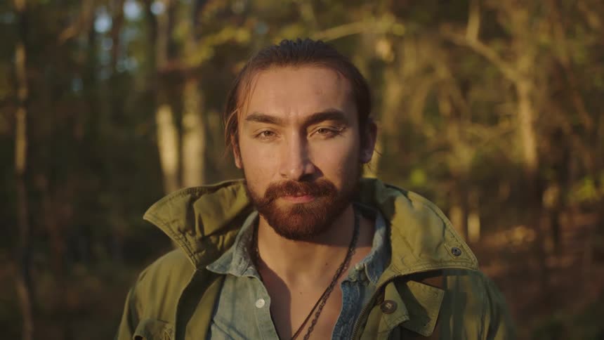 A man with a jacket standing and staring in a forest with plants and trees in the background