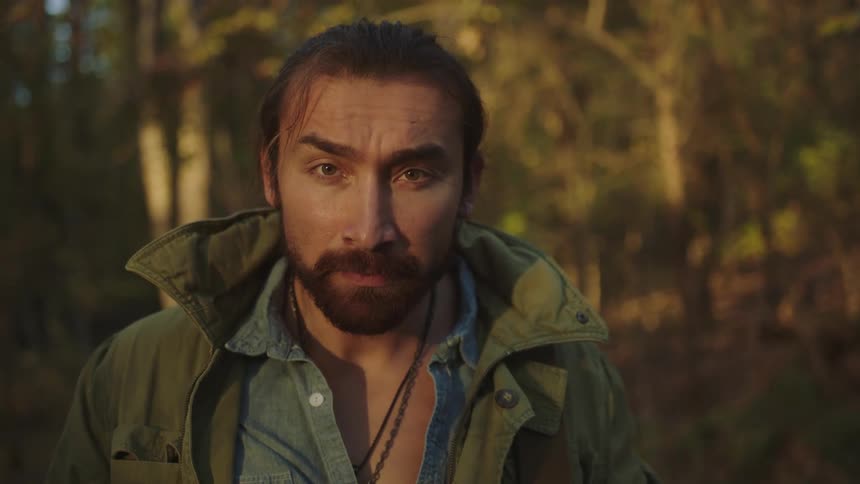 A man standing in a forest raises his head to look into the camera