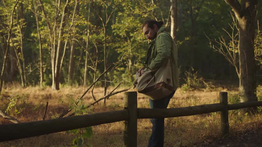 A hiker stops along a fence in the woods to check his tablet