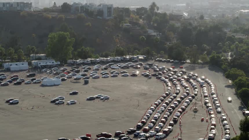 Cars wait in long lines for covid testing and vaccines with a city skyline behind