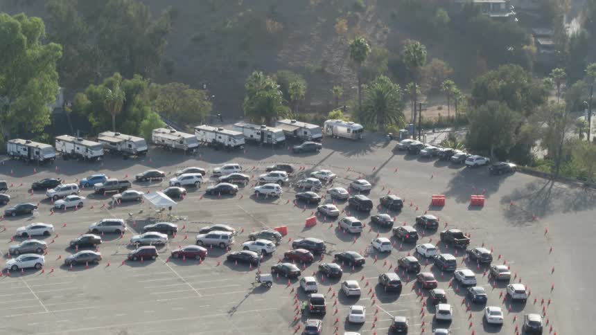 Rows of cars line up in a large parking lot near the city