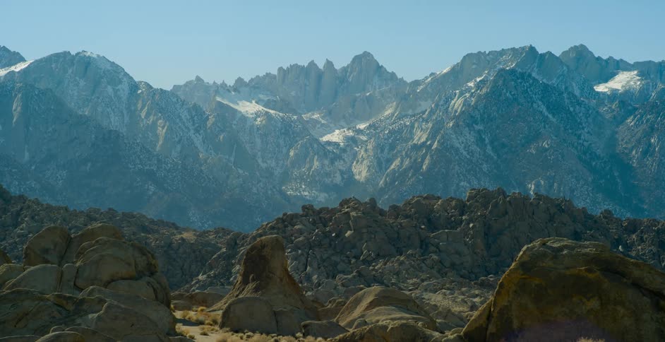 Large boulders and ridged hills sit below a mountain range